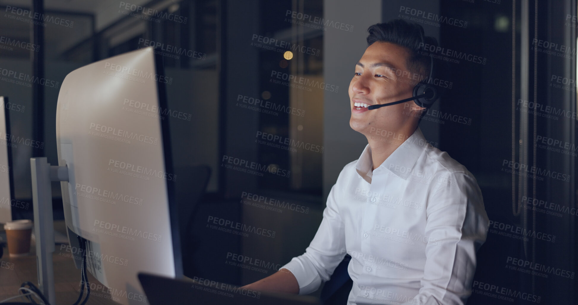 Buy stock photo Callcenter, night and Asian man in office with phone call, computer and headset in communication with smile. Telemarketing, customer service or crm, happy help desk consultant for night support work