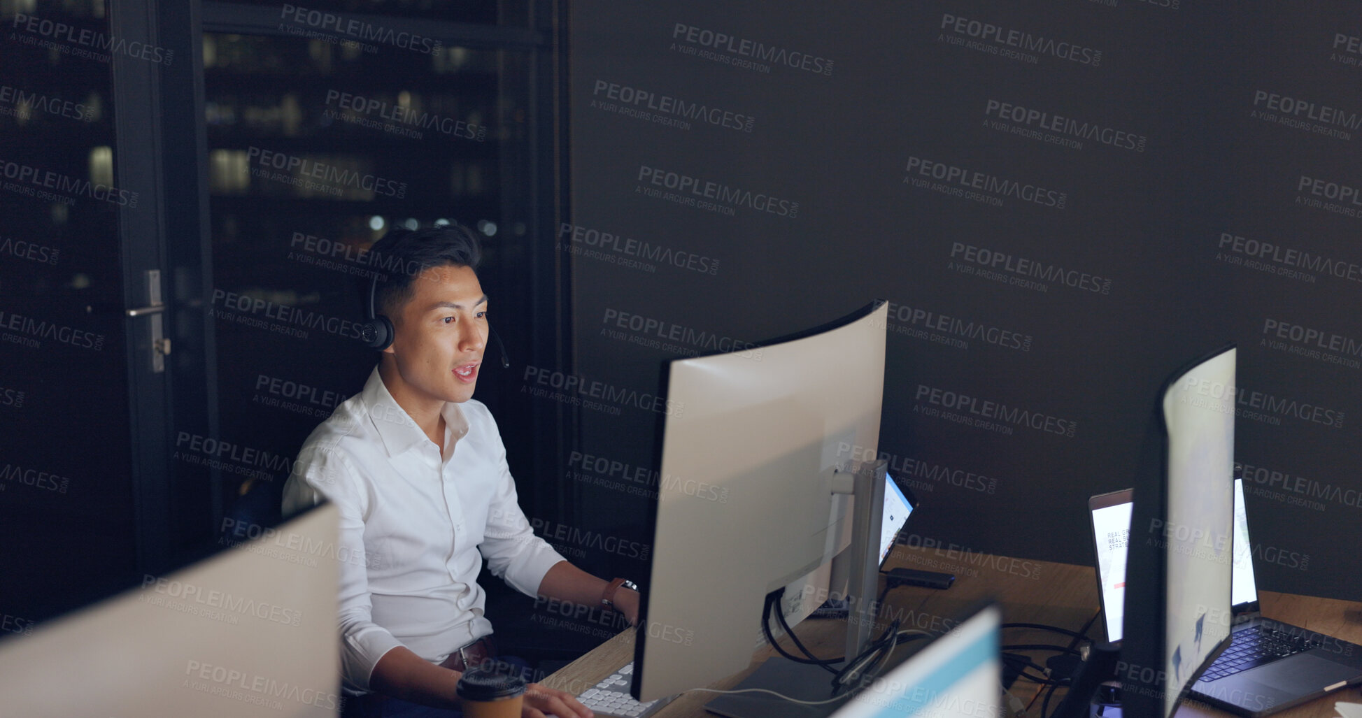Buy stock photo Customer service, night and Asian man at desk with phone call, computer and headset in communication in overtime. Telemarketing, call center and crm, tech support consultant for night work in office.