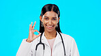 OK hand and woman doctor isolated on blue background for healthcare success and service support. Like, yes and agreement sign or emoji of Indian person or medical worker face or portrait in studio
