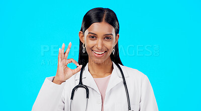 Buy stock photo Happy woman, portrait and doctor with OK sign for healthcare success against a blue studio background. Female person, surgeon or medical professional smile with okay emoji, perfect or yes sign