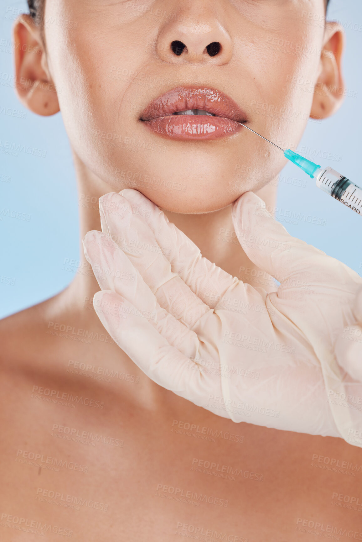 Buy stock photo Closeup of a young woman getting lips injection treatment from a cosmetic doctor in a studio. Syringe and needle with lip filler for the mouth by a cosmetology beautician with a blue background