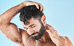 Hair care, face and water splash of man in shower in studio isolated on a blue background. Water drops, dermatology and male model washing, cleaning or bathing for skincare, wellness and hygiene.