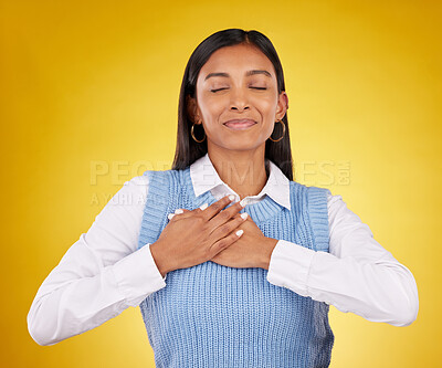 Buy stock photo Gratitude, peace and young female in a studio with her hand on her chest for a grateful expression. Mindfulness, smile and Indian woman model with thankful gesture isolated by yellow background.