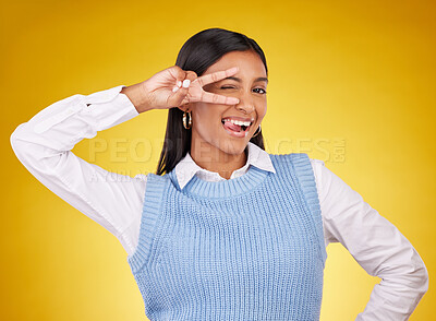 Buy stock photo Peace sign, hands and portrait of Indian woman wink in studio for happiness, confident and fashion. Emoji mockup, yellow background and girl with hand gesture for joy, positive mindset and happy