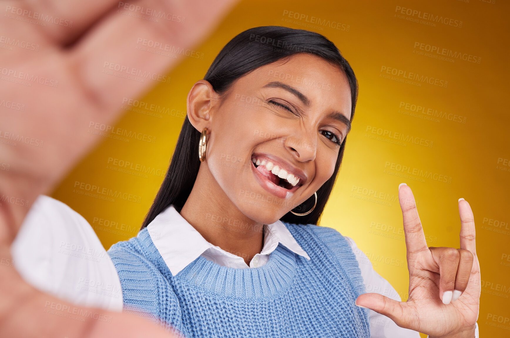 Buy stock photo Selfie, rock sign and portrait of Indian woman in studio for happiness, confident and wink on yellow background. Mockup, fashion and girl with punk hand gesture with beauty, cosmetics and makeup