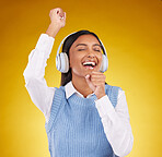 Headphones, energy and female singing in studio while listening to music, playlist or album. Happy, smile and Indian woman model doing karaoke while streaming a song isolated by yellow background.