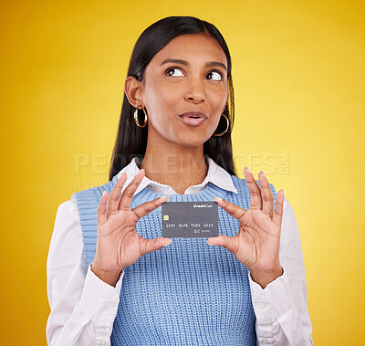 Buy stock photo Credit card, thinking and Indian woman on yellow background for bank, investment and payment in studio. Banking mockup, finance and happy girl with plastic for budget, commerce and discount purchase