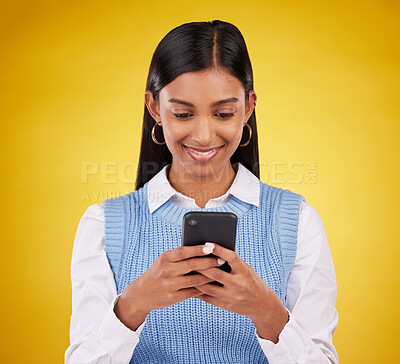 Buy stock photo Smile, phone and happy woman in studio typing message, email or web post on yellow background. Technology, communication and happy Indian gen z girl influencer checking social media or online content