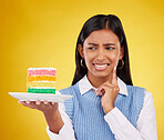 Upset woman, rainbow cake and studio while thinking of birthday celebration, disaster or mistake. Face of Indian gen z female with dessert food with color, foul smell or bad idea on yellow background