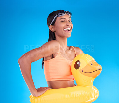 Buy stock photo Portrait, wink and rubber duck with a woman on a blue background in studio excited for summer. Happy, smile and playful with an attractive young female ready for swimming on holiday or vacation