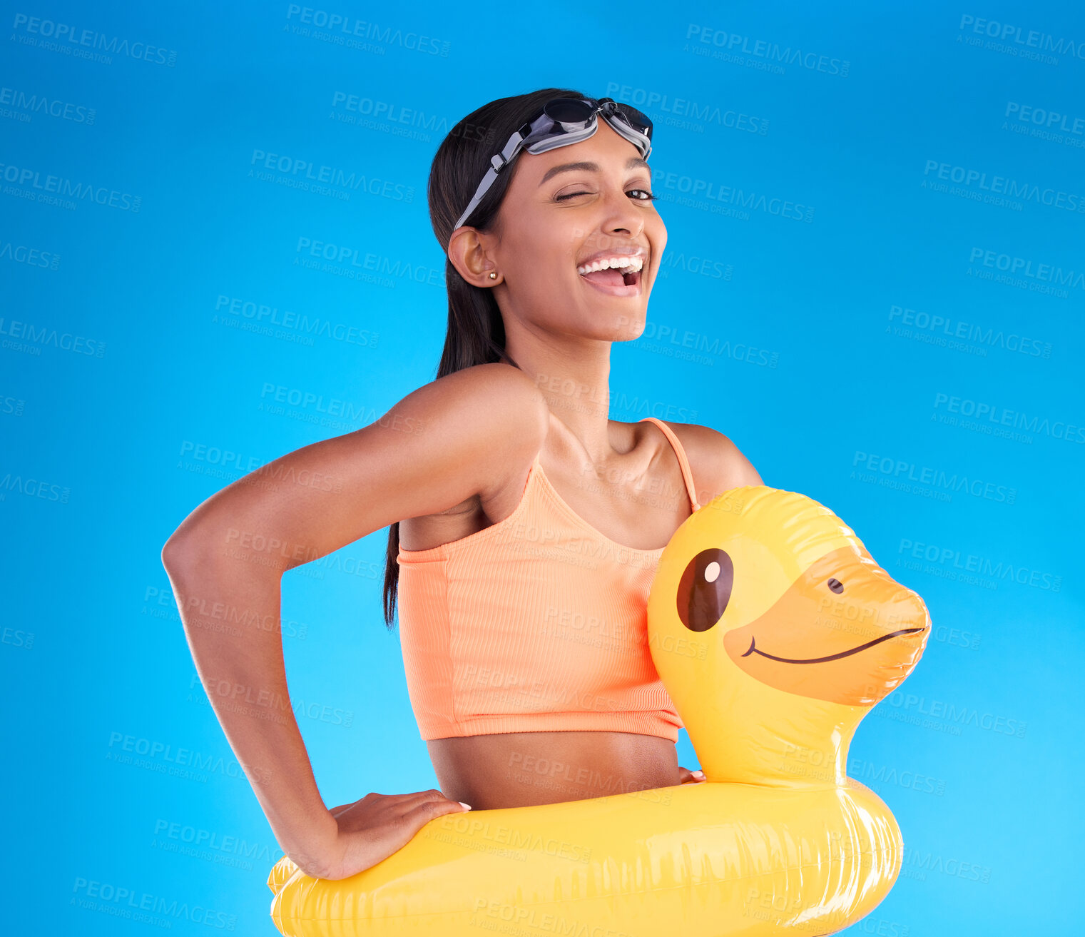 Buy stock photo Portrait, wink and rubber duck with a woman on a blue background in studio excited for summer. Happy, smile and playful with an attractive young female ready for swimming on holiday or vacation