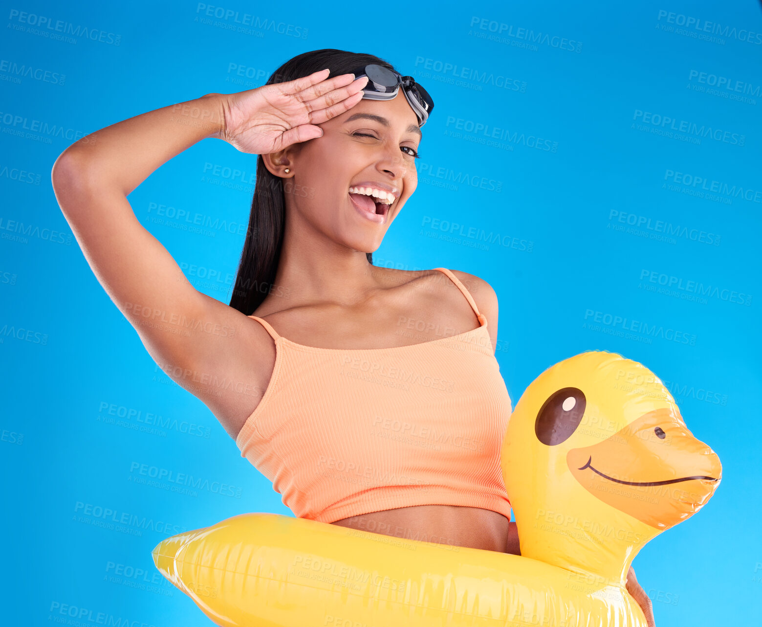 Buy stock photo Portrait, smile and salute with a swimmer woman in studio on. a blue background wearing goggles on her head. Happy, hand gesture and swimming with an attractive young female excited to swim in summer