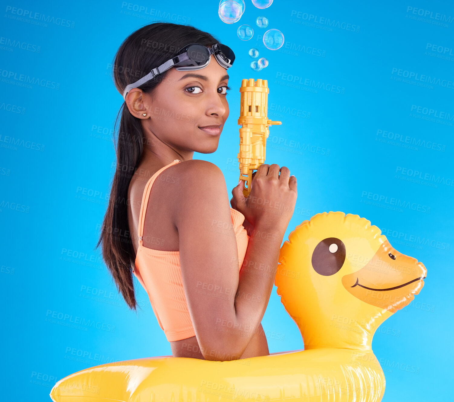 Buy stock photo Portrait, bubbles and rubber duck with a woman on a blue background in studio ready for summer swimming. Happy, travel and vacation with an attractive or playful young female holding a bubble gun