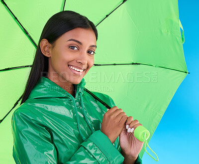 Buy stock photo Portrait, smile and female with an umbrella in a studio with a stylish, trendy and fashion green rain coat. Life insurance, face and Indian woman model with winter outfit isolated by blue background.