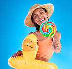 Portrait, lollipop and inflatable duck with a woman on a blue background in studio ready for summer swimming. Happy, travel and vacation with an attractive young female looking excited to relax