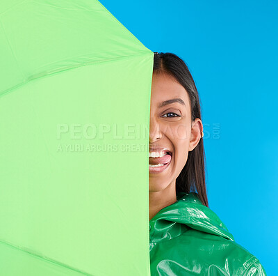 Buy stock photo Umbrella, silly and woman portrait with tongue out in studio with raincoat and happiness. Fun, face and playful young female in isolated blue background with comedy, emoji and funny joke with a smile