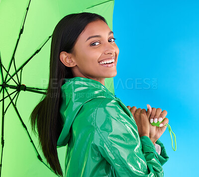 Buy stock photo Happy, portrait and woman with an umbrella in studio with a stylish, trendy and fashion green rain coat. Life insurance, smile and Indian female model with a winter outfit isolated by blue background