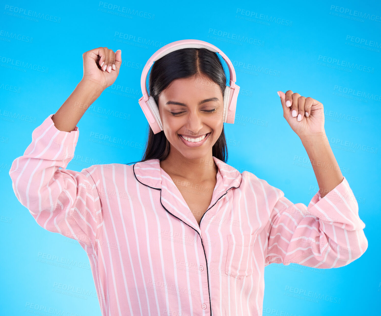 Buy stock photo Happy, dance and woman in pajamas, headphones and cheerful on a blue studio background. Female, joyful and lady with headset, waking up and dancing with sounds, streaming music and songs for movement