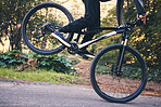Closeup man, mountain bike and wheel for cycling stunt in park, nature and path for fitness, cardio and freedom. Bicycle, cyclist and extreme sports athlete training for action, wheelie stunt or risk