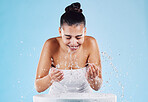 Sink, water splash and happy skincare of a woman washing face for natural beauty and facial wellness. Isolated, blue background and studio with a female model doing dermatology and cosmetic routine
