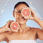 Skincare, grapefruit and mature woman in studio for a natural, beauty and organic face routine. Cosmetic, water splash and female model with a citrus fruit for wellness isolated by a blue background.