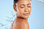 Water splash, skincare and woman on blue studio background health, wellness and hygiene with cleaning routine. Shower, cosmetic beauty and relax, mature model in skin care or dermatology treatment.