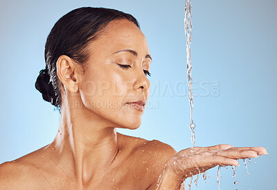 Buy stock photo Mature, grooming and a woman catching water for beauty isolated on a blue background in a studio. Skincare, hygiene and a model in the shower for morning routine, body care and washing on a backdrop