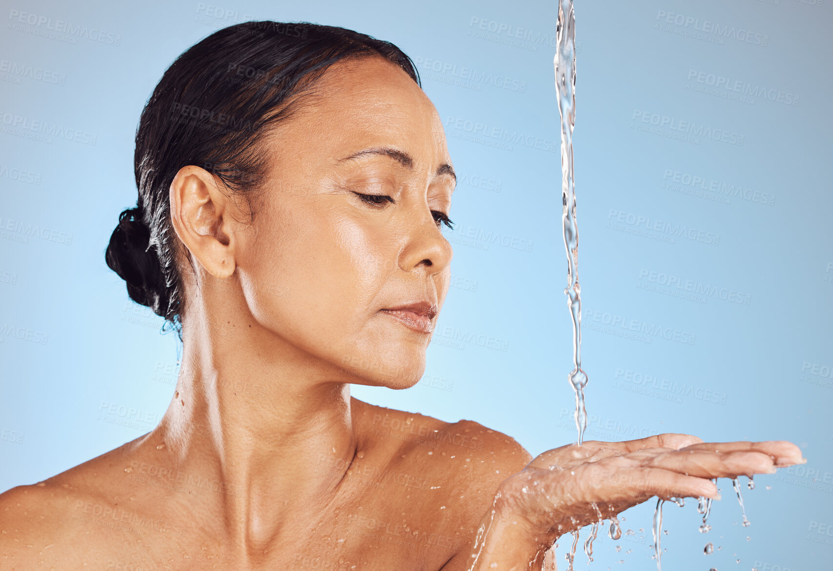 Buy stock photo Mature, grooming and a woman catching water for beauty isolated on a blue background in a studio. Skincare, hygiene and a model in the shower for morning routine, body care and washing on a backdrop