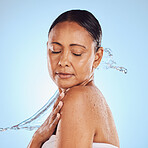 Skincare, shower and a mature woman with a water splash isolated on a blue background in a studio. Glow, anti aging and a model with hydration, liquid and fluid for skin, grooming and hygiene