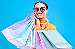 Retail bags, studio and woman portrait with a smile and happiness from boutique sale. Happy, shopping and female model with store bag and sales choice in isolated blue background with sunglasses
