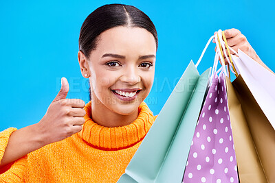Buy stock photo Happy woman, portrait smile and shopping bags with thumbs up for purchase, sale or discount against blue studio background. Face of female shopper with gift bag showing thumb emoji, yes sign or like