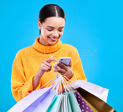 Buy stock photo Happy woman, phone and shopping bags with smile for purchase, sale or discount against a blue studio background. Excited female shopper smiling on mobile smartphone holding gift bag for social media