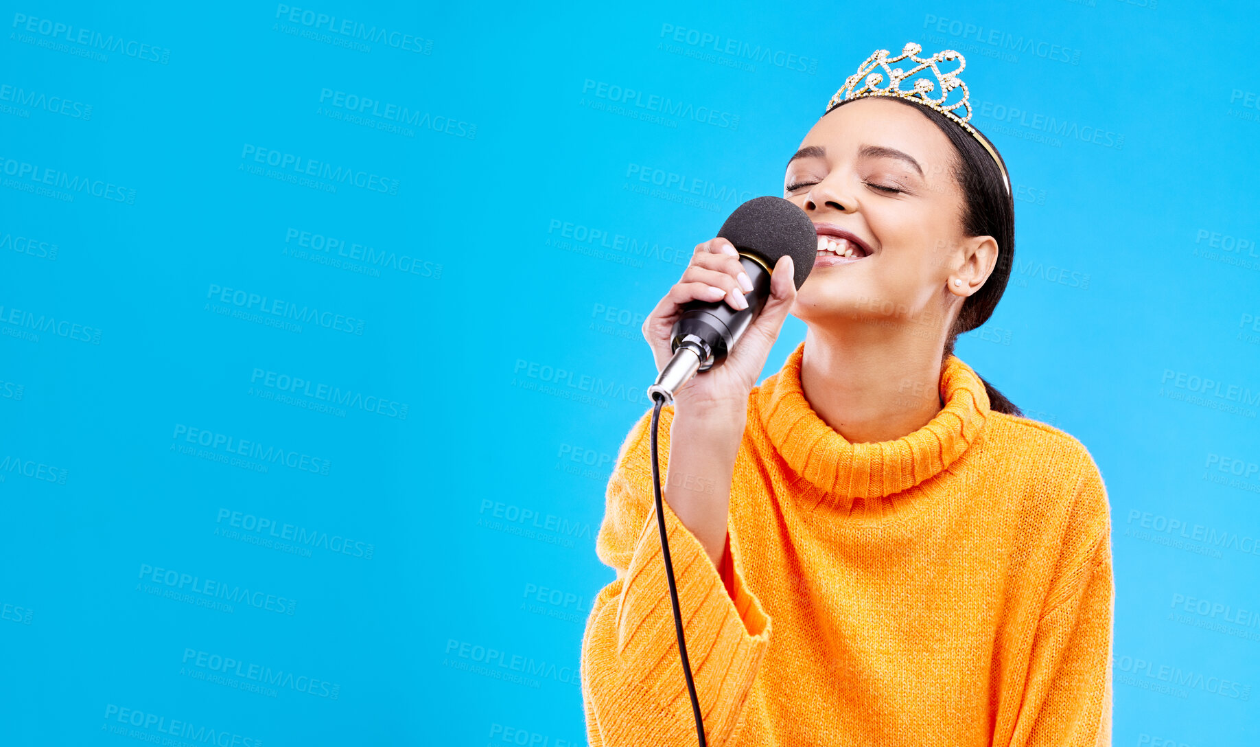 Buy stock photo Singer woman, crown and microphone in studio mockup with smile for singing performance by blue background. Happy gen z girl, model or recording artist mic for karaoke, music and mock up with tiara