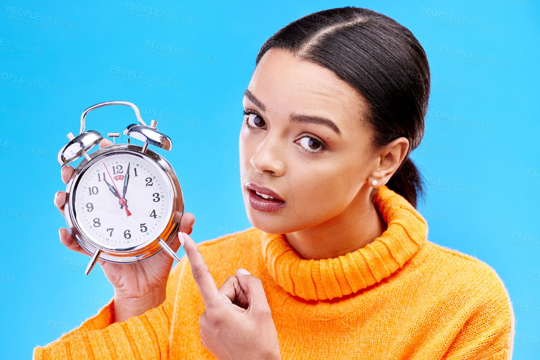 Buy stock photo Woman, annoyed and point at alarm clock in portrait for warning by blue background in studio. Gen z girl, student and model with watch, time management and schedule with angry face to start morning