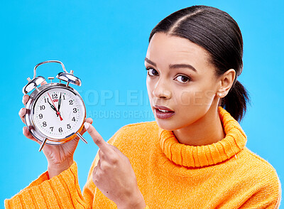 Buy stock photo Woman, annoyed and pointing at alarm clock in portrait for warning by blue background in studio. Gen z girl, student or model with watch, time management and schedule with angry face to start morning