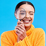 Smile, portrait and woman with a magnifier in a studio for an investigation or detective cosplay. Happiness, excited and headshot of a female model with a magnifying glass isolated by blue background