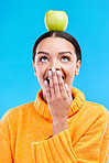 Apple head balance, woman face and surprised with fruit product for weight loss benefits, healthy lifestyle or body detox. Organic food diet, nutritionist studio and shocked person on blue background