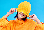 Fashion, happy and hide with woman and beanie in studio for cover, winter and goofy. Playful, happiness and smile with female and knitted hat isolated on blue background for funny, silly and cool