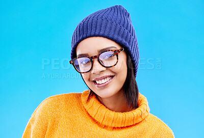 Buy stock photo Portrait of woman in winter fashion with smile, beanie and glasses isolated on blue background. Style, happiness and gen z girl in studio backdrop with happy face and warm clothing for cold weather.