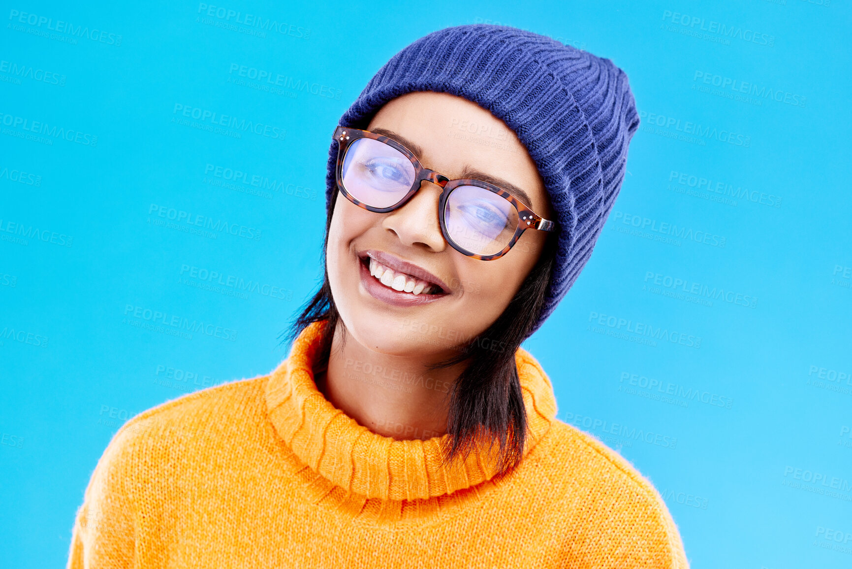 Buy stock photo Portrait of happy woman in winter fashion with glasses, beanie and smile isolated on blue background. Style, happiness and face of gen z girl on studio backdrop with warm clothing for cold weather.