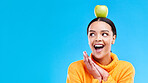 Wow, apple on head and a woman in studio on a blue background for product placement on mockup. Surprise, balance and space with an attractive young female posing to promote health, diet or nutrition