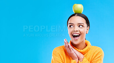 Buy stock photo Wow, apple on head and a woman in studio on a blue background for product placement on mockup. Surprise, balance and space with an attractive young female posing to promote health, diet or nutrition