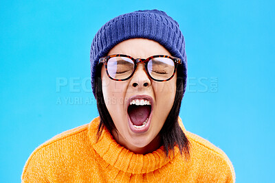 Buy stock photo Portrait of woman in winter fashion, screaming with beanie and glasses isolated on blue background. Anger, frustration and face of frustrated gen z girl in studio with warm clothes for cold weather.