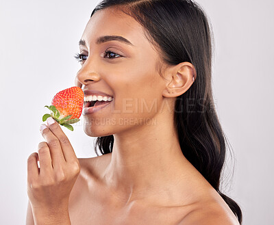 Buy stock photo Happy, healthy and a woman eating a strawberry for nutrition isolated on a white background in a studio. Smile, thinking and an Indian girl with a fruit for a diet, breakfast or vitamins from food