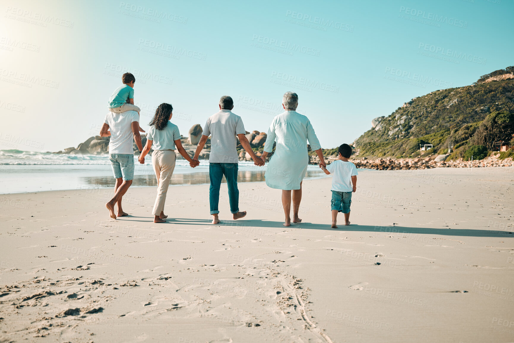 Buy stock photo Family, walking and holding hands outdoor on a beach with children, parents and grandparents together. Men, women and boy kids walk at sea with love, care and quality time for summer travel vacation