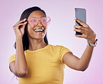 Sunglasses, selfie smile and Indian woman on pink background with cosmetics, confidence and beauty. Fashion, smartphone and girl in studio take picture for social media, post and influencer blog