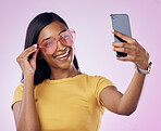 Sunglasses, selfie and happy Indian woman on pink background with cosmetics, confidence and beauty. Fashion, smartphone and girl in studio take picture for social media, post and influencer blog