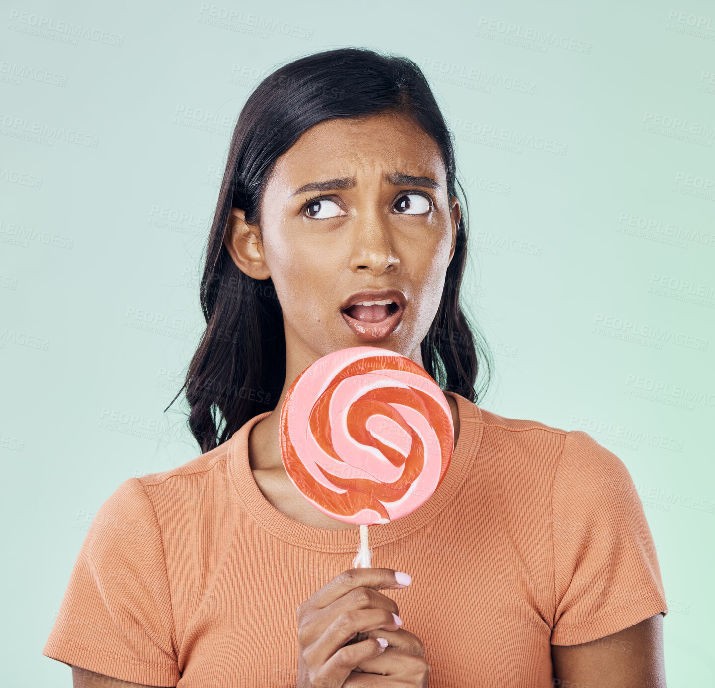 Buy stock photo Thinking, lollipop and woman with candy in studio isolated on a green background. Idea, sweets and Indian person with snack, delicious sucker or sugar treats, dessert or confectionery junk food.