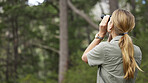 Binoculars, forest explore and woman in nature, travel journey or outdoor adventure for carbon footprint research. Rear watch, search and person birdwatching in jungle, woods or eco green environment