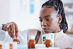 Serious black woman, patient and medication on shelf for cure, illness or pain relief at pharmacy. African American female reading or looking at pharmaceutical products, medicine or drugs at clinic